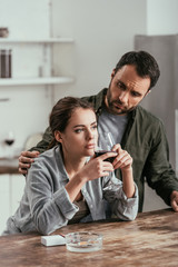 Man looking at pensive wife with wine glass at kitchen