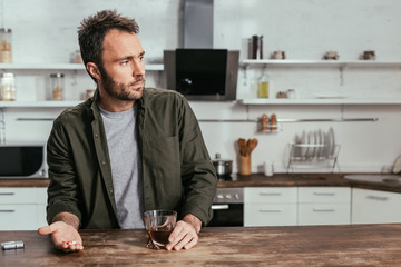 Sad man holding whiskey glass and pills on kitchen table