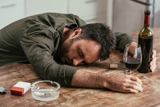 Drunk man sleeping on table with wine and cigarettes