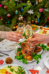 Human hands holding glasses with sparkling wine. Friends or family toasting with champagne against festive Christmas table and decorated new year tree. Winter holidays celebration at cozy home