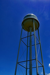 Tall Water tower with sun overhead with bright dark blue sky in background