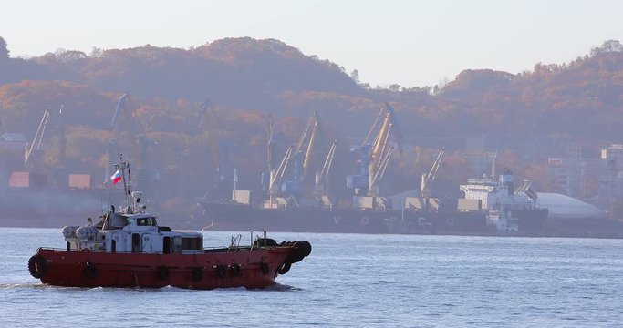 City of Nakhodka. A small red tugboat goes on Nakhodka Bay on the background of coal ports