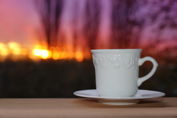 white cup with coffee, tea on a background of dark evening purple sunset among the branches of trees