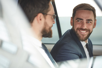Young happy businessman talking to his colleague and smiling while they sitting in the car