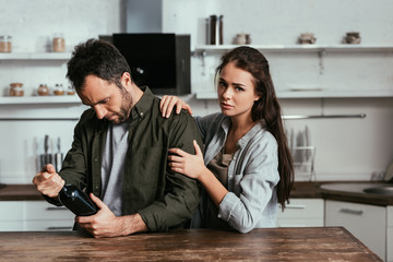 Woman stopping alcohol addicted husband with wine bottle