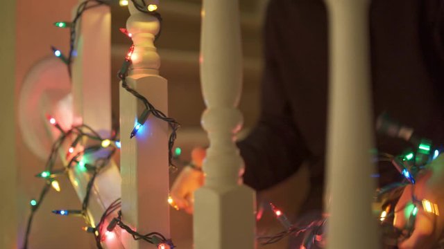Little boy hanging Christmas lights on railing in house