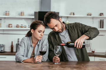 Alcohol dependent couple pouring red wine on kitchen