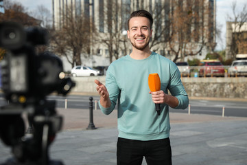 Young male journalist with microphone working on city street