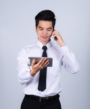 Portrait handsome young asian man wearing a white shirt takling telephone and holding tablet smile and happy isolated on gray background in studio. Asian man people. business success concept.