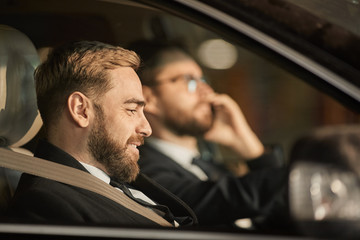 Side view of young bearded passenger smiling while sitting in the car with driver driving the car