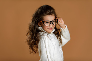 Cute curly little child girl wearing glasses and looking to camera in studio
