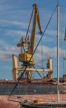 Industrial Crane. Big yellow crane with sailboat in the front of photo and sky with clouds in the background. Stock image.