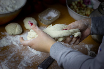 A piece of dough in the hands of a woman for making a pie. On the table are prepared for baking buns with slices of apple stuffing.