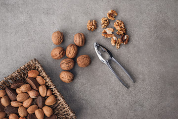 Whole and peeled walnuts, almonds and pecans in a wicker basket on a stone surface. Gray background. Top view.