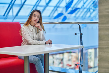 young woman in a shopping center sitting at a table in a cafe on a red sofa