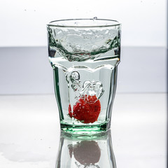 In the glass with clean and transparent water, falls fresh strawberries, splashes water.