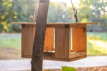 Wooden bird feeder house on a tree in autumn park. Animal wildlife care concept.