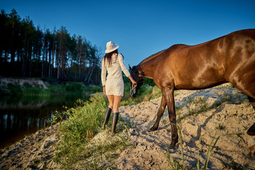 a woman in white dresses and white hats at sunset on a summer evening led the horse to the lake....