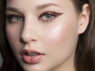 Beautiful woman with bright make up eye with sexy red liner makeup. Fashion big arrow shape on woman's eyelid. Natural lips. Chic evening make-up. Luxurious long wave hair. Shining face skin