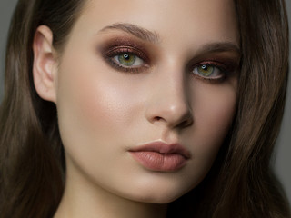 Close-up portrait of beautiful woman's purity face with dark green smoky-eyes make-up, pale full lips. Sexy model with clean shiny skin, purity complexion