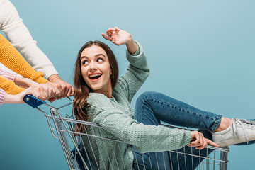 friends having fun and riding emotional girl in shopping cart, isolated on blue