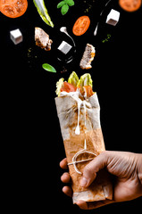 Shawarma\chicken pita\roll in a hand with ingredients fly in the air on black background
