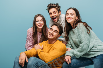 smiling friends having fun with shopping cart, isolated on blue