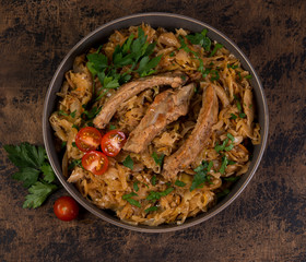 Bigos of stewed sauerkraut with pork ribs. Traditionally the Polish dish in a plate decorated with greens and tomatoes stands on a wooden table. Top view.