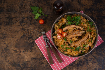 Bigos of stewed sauerkraut with pork ribs. Traditionally the Polish dish in a plate decorated with greens and tomatoes stands on a wooden table on the right. Top view with copy space.