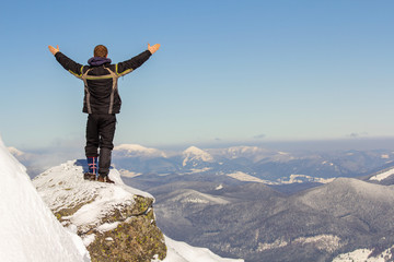 Silhouette of alone tourist standing on snowy mountain top in winner pose with raised hands enjoying view and achievement on bright sunny winter day. Adventure, outdoors activities, healthy lifestyle.