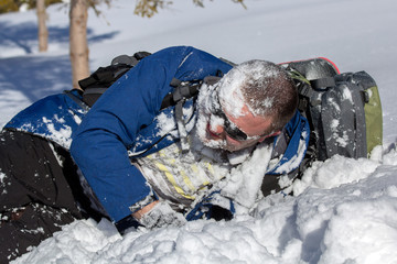 Hiker in sunglasses with backpack lay down with snow on his face in winter.