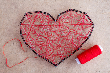 Close up of a red heart made of threads wound between nails. The concept of confused feelings in humans.