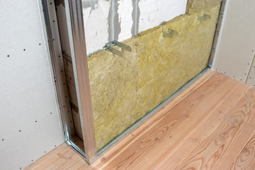 Wall of a room under renovation with mineral rock wool insulation and metal frame prepared for drywall plates.