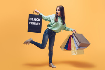 shocked girl holding shopping bags on black friday, on yellow
