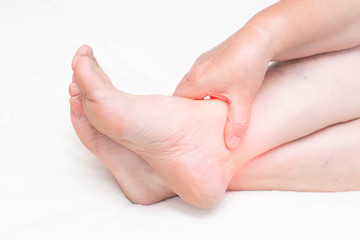 An elderly woman holds on to the ankle joint in the leg in which pain and inflammation. The concept of ankle disease and arthrosis and arthritis of the joint, sprain, close-up.