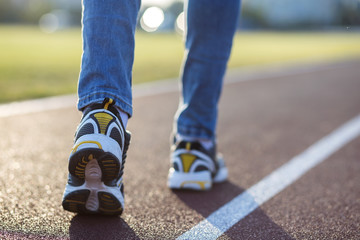 Fototapeta na wymiar Close up of woman feet in sport sneakers and blue jeans on running lane on outdoor sports court.