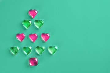 Christmas tree made of pink and green decorative glass hearts laying on trendy mint background. Minimal flat lay 2020 New Year holiday concept. Copy space for text.