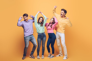 Fototapeta premium excited young friends dancing together, on yellow
