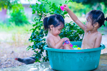 Two Asian girls kindergartens are having fun playing in the water bath.