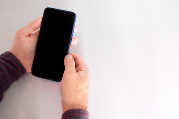 holding a mobile phone with a blank black screen. reads from a smartphone on a light background with place for text mockup