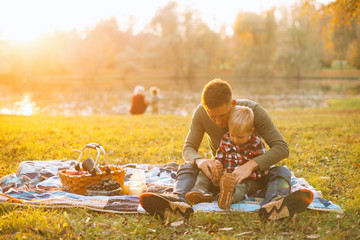 A dad and his son are having picnic together near a lake in park.