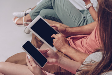 cropped view of friends using digital devices with blank screens while sitting together isolated on grey