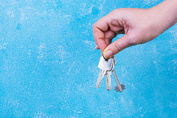 Female hand holding keys on blue background