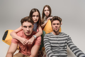 worried friends sitting on bin bag chair together, on grey