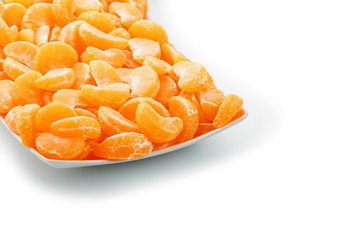 Slices of juicy tangerines in a white plate on a white background.