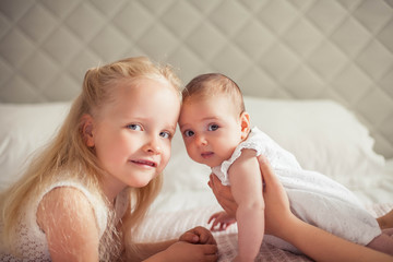 Young beautiful mother holds a baby. Little sister kisses her little sister. Baby. Children bedroom.