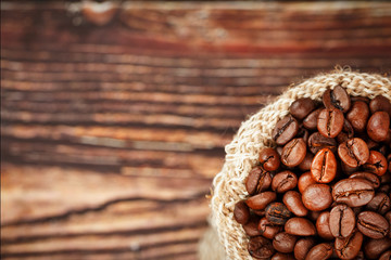 Coffee beans closeup in burlap bag on wooden background.