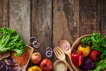 Top table salad bowl with full of salad inside and a lot of ingredient around the bowl. All are on a wooden table include big spoon and fork with typing space on the top area of image.