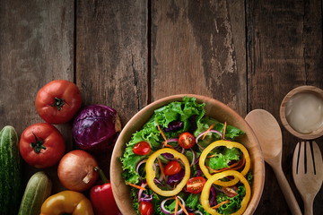 Top table salad bowl with full of salad inside and a lot of ingredient around the bowl. All are on a wooden table include big spoon and fork with typing space on the top area of image.