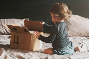 Little child playing with cardboard box on bed. Orders delivered by mail from international retail...